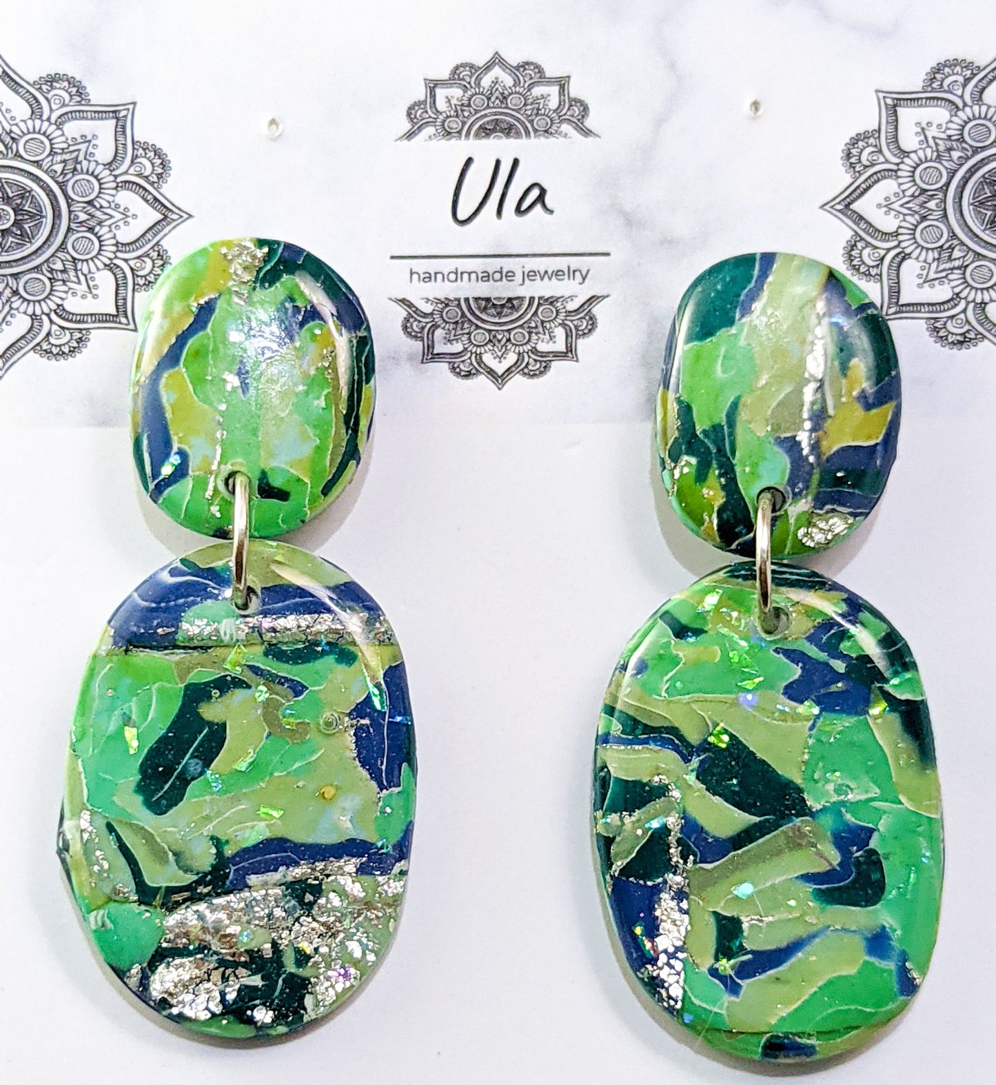 Pair of green and blue patterned earrings on a branded card.
